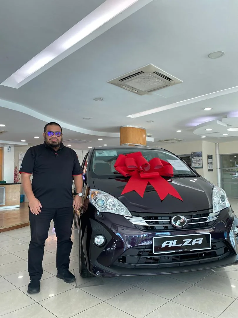 Sales Advisor Perodua 3S Elmina berdiri bersama kereta Perodua dan reben merah di showroom